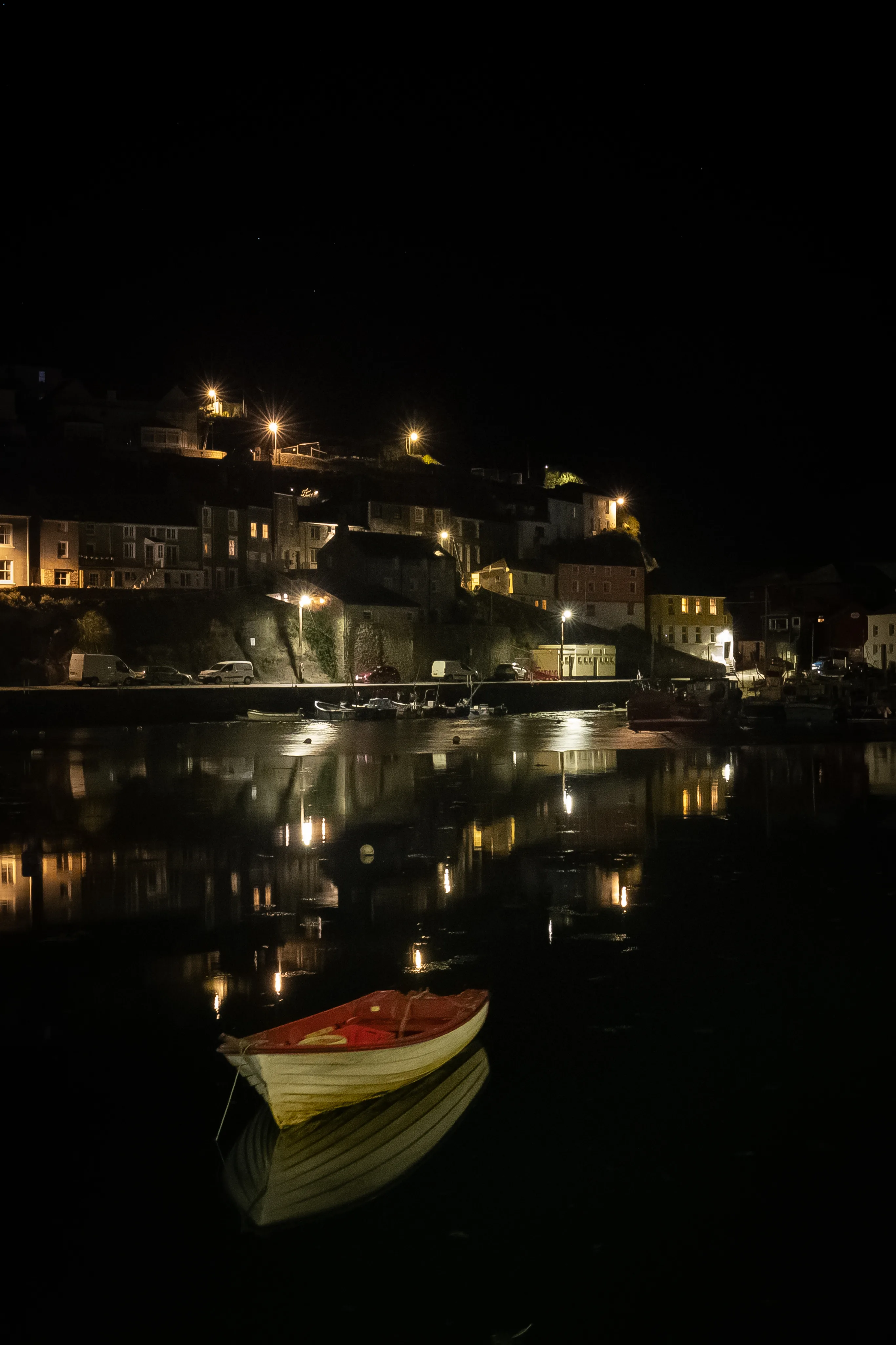 Small boat resting on still water beneath the lights of a coastal village at night