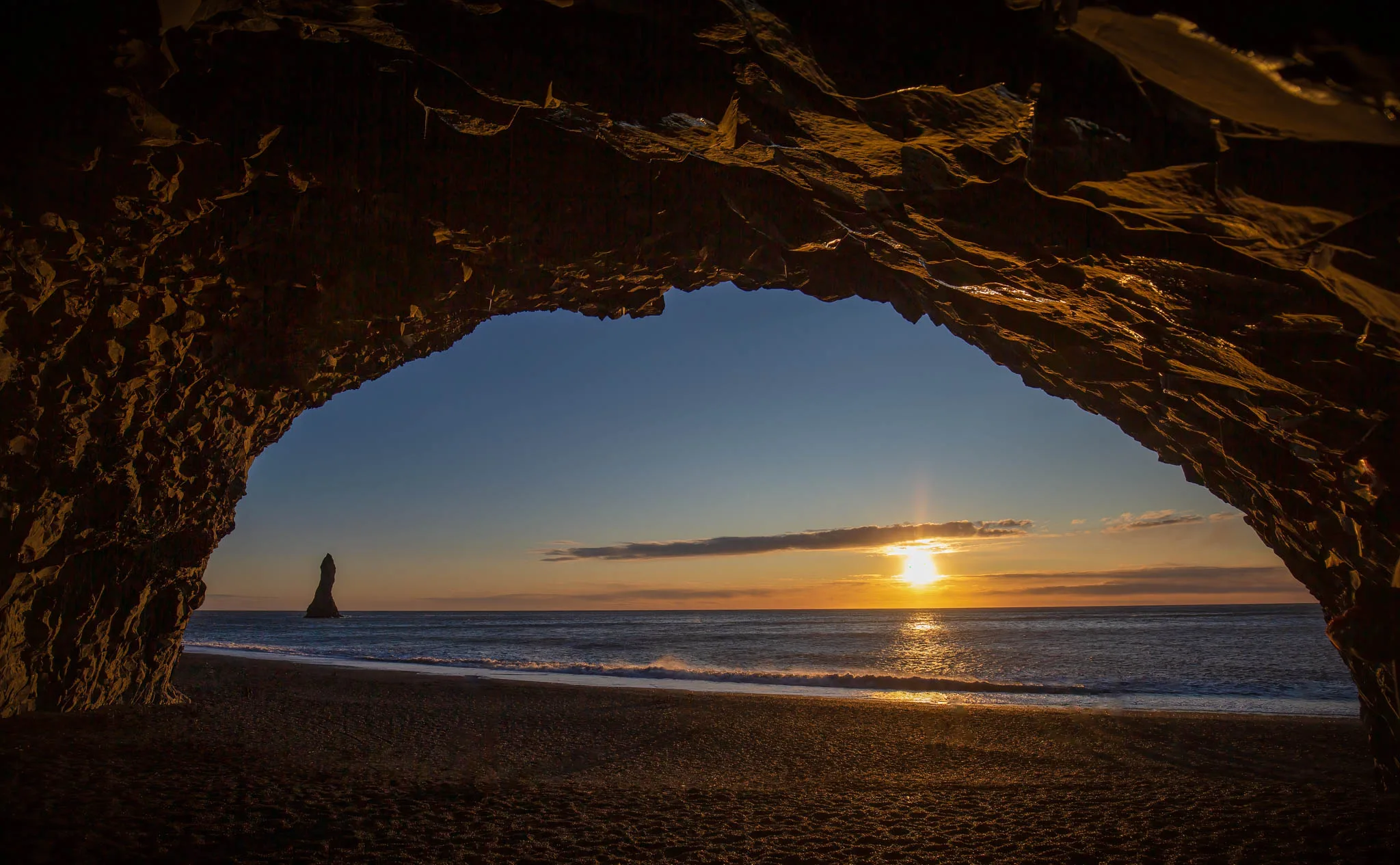 Setting sun framed by a rocky coastal arch overlooking the sea
