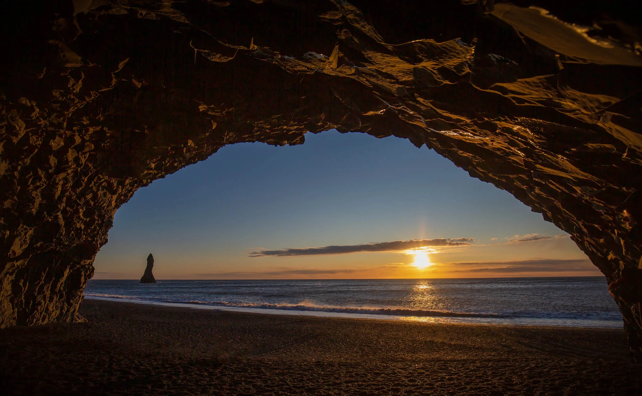 Setting sun framed by a rocky coastal arch overlooking the sea