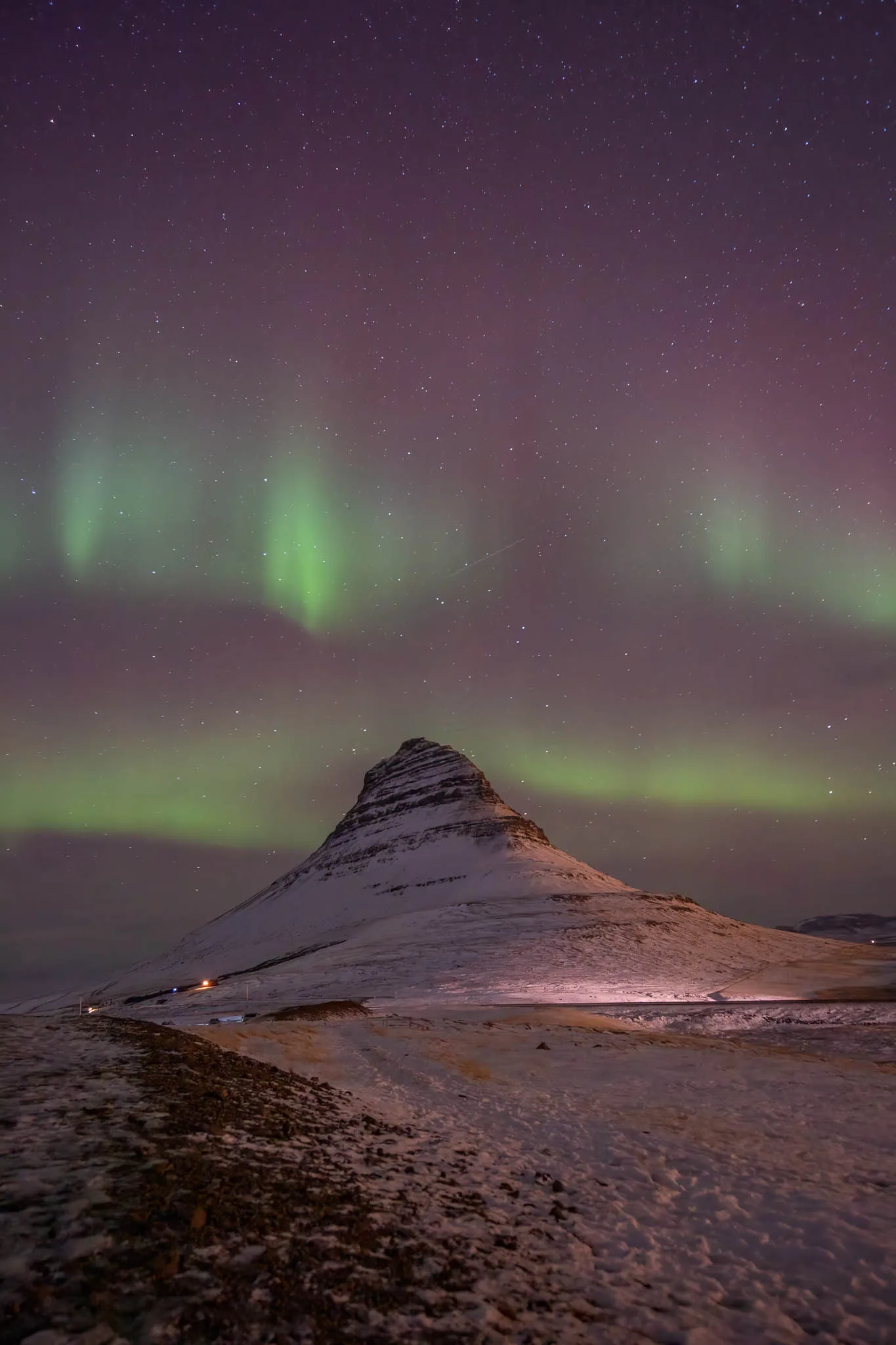 Portrait photograph of Kirkjufell mountain beneath purple and green northern lights