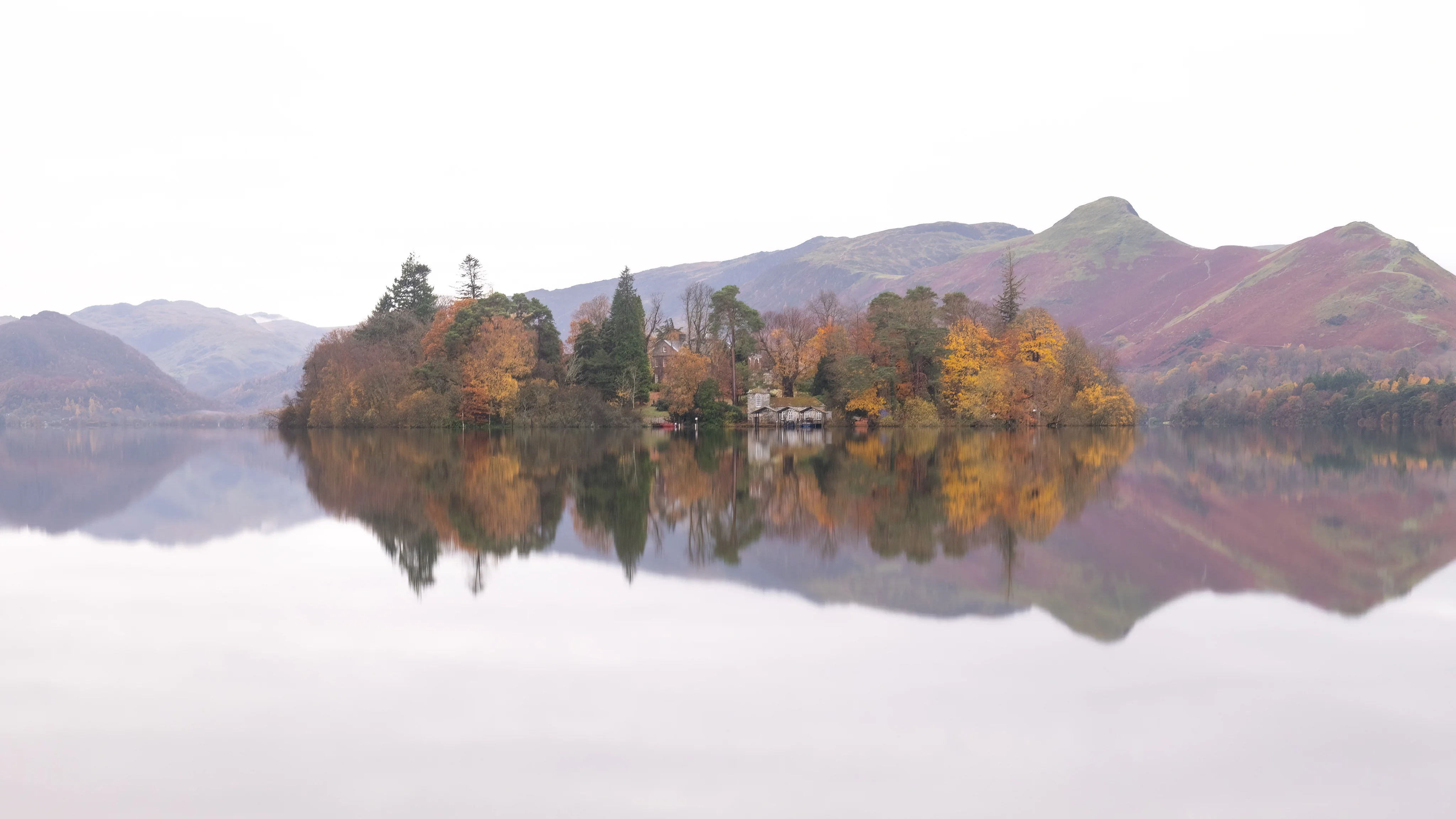 Autumn-coloured trees on a small island reflected in a mountain lake