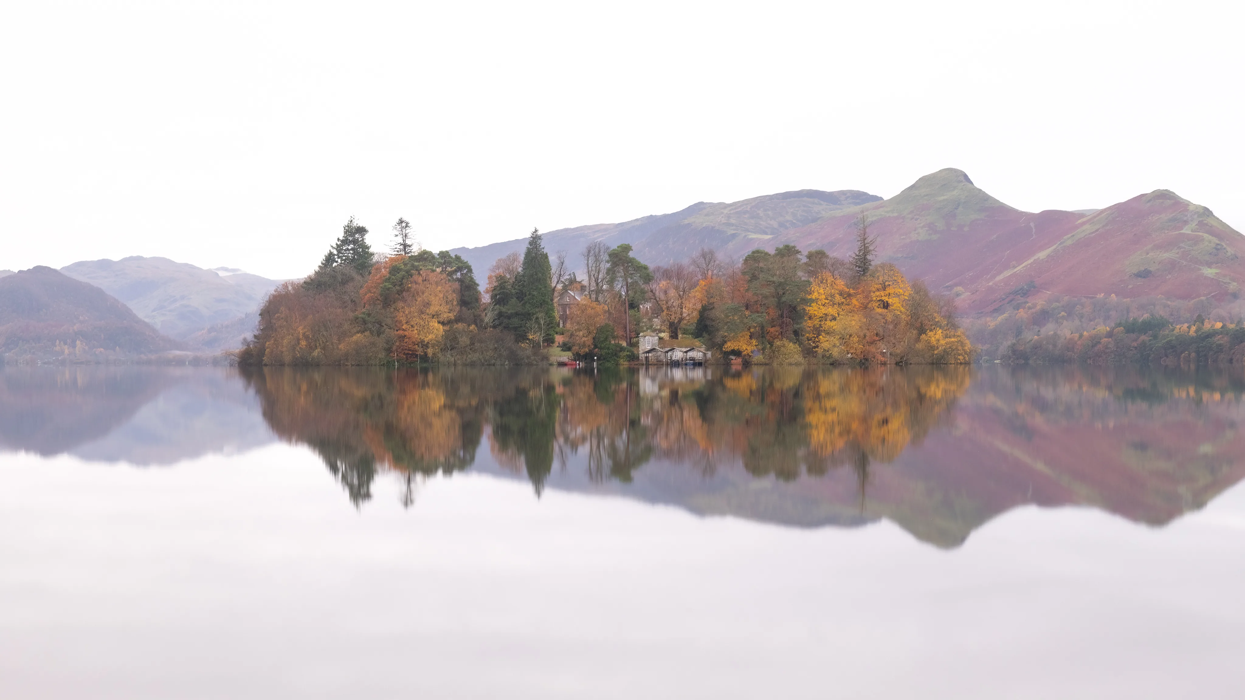 Autumn-coloured trees on a small island reflected in a mountain lake