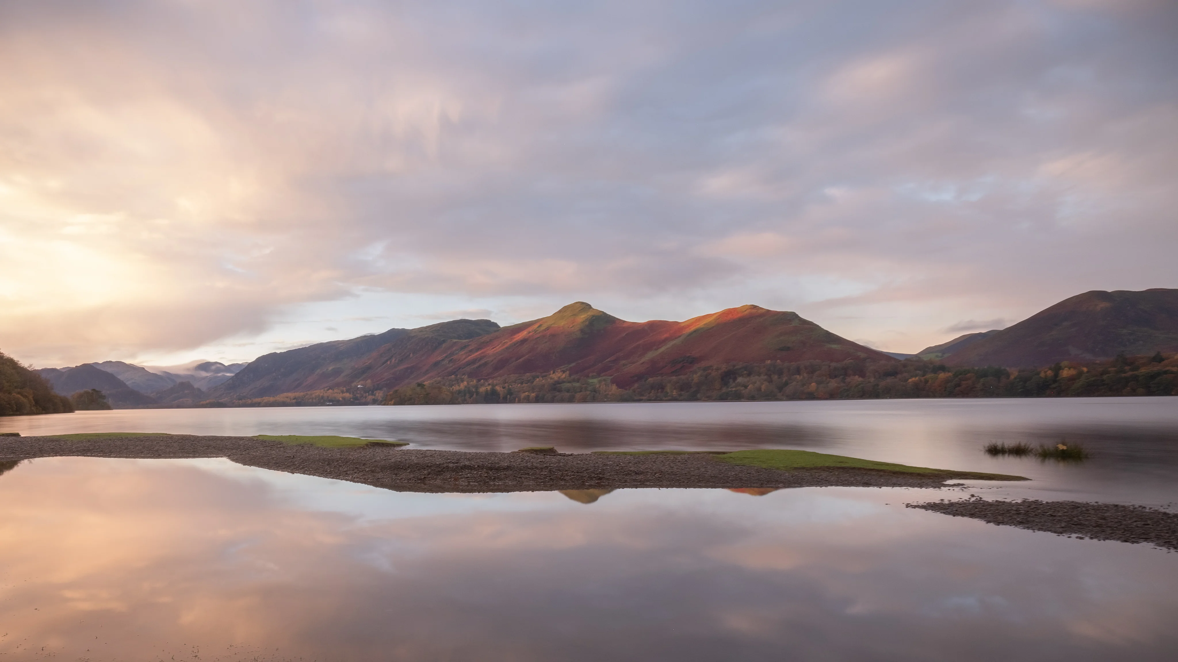 Soft morning light illuminating mountains reflected in a tranquil lake